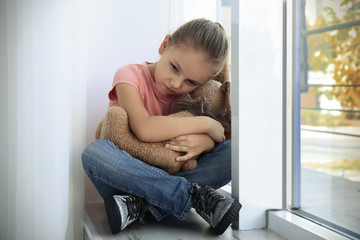 Little sad girl with toy at home. Abuse of children concept