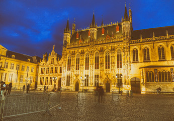 Fototapeta na wymiar BRUGES, BELGIUM - MARCH 2015: Tourists visit ancient medieval Burg Square at night. Brugge attracts more than 2 million people annually