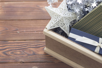 An edge of a wooden box filled with a white patterned star, silver garland, a green striped box and a blue gift box with a white satin ribbon. Rustic wooden background.