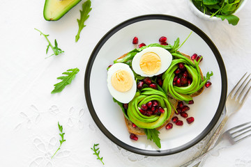 Toast with avocado rose, boiled egg and fresh salad on white table cloth