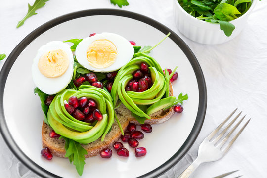 Toast with avocado rose, boiled egg and fresh salad on white table cloth