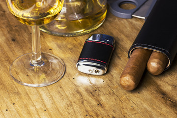 Leather case with cigars, bottle and glass of whiskey, lighter and cigar cutter on an wooden board