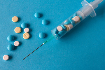 Pills in a syringe and series on a blue background with copy space close-up