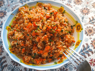 Risotto with peppers, carrots and tomatoes on the plate, delicious vegetarian food.