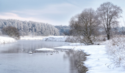 Morning frosty winter landscape with dazzling white snow on the banks and the blue sky. Foggy river bank with frost covered.