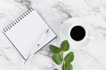 cup of coffee beside a note pad and pen on a marble background