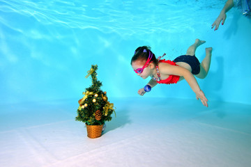 Child underwater dives to the bottom of the pool to a Christmas tree with the toy in his hand....