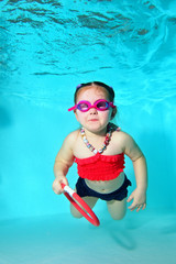 Little girl swims underwater in the pool on a blue background, looking at camera and smiling. Portrait. Shooting under water. Vertical orientation