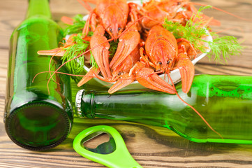 Lot of boiled red crayfishes and green fresh dill in white ceramic bowl beside two full bottles of...