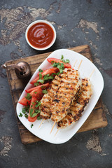Lula kebabs with chicken meat, fresh vegetables and sauce on a rustic wooden serving board, flat-lay on a brown stone background