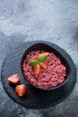 Risotto with strawberries in a bowl on a stone slate tray, vertical shot with copy space over gray concrete background