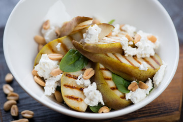 Salad with grilled pears, feta cheese, nuts and spinach leaves served in a white bowl, close-up