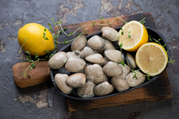 Metal plate with raw fresh vongole clams and lemons on a rustic wooden chopping board, studio shot