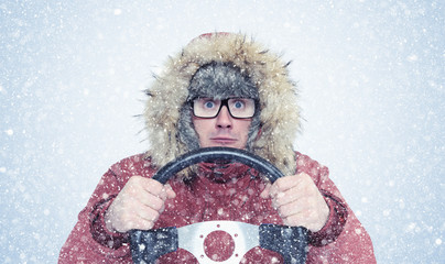 Man in winter clothes with a steering wheel, snow, blizzard. Concept car driver 
