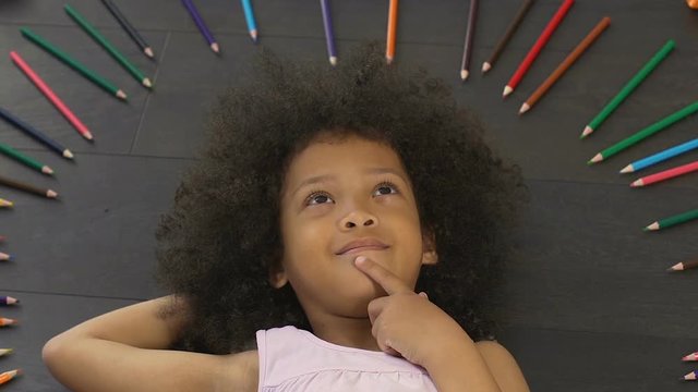 Small kid with big afro lying on floor and thinking of new idea, imagination