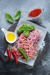 Top view of raw pork mincemeat with cooking ingredients, gray concrete background, vertical shot