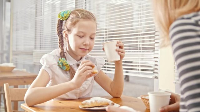 Girl with pigtails eats cakes and drinks with her mum in the cafe
