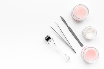 Desk of cosmetoligist. Dermaroller, creams and mask, tools on white background top view copyspace