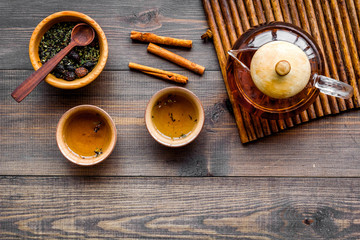 Obraz na płótnie Canvas Accessories for tea ceremony. Tea pot, cups, dry tea leaves on dark wooden background top view copyspace