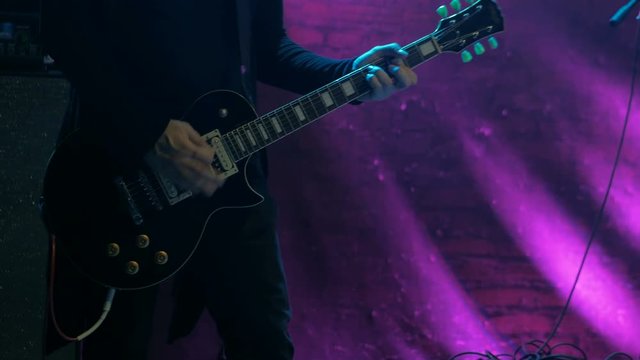Close up shot of man playing guitar on concert stage. Purple light. Entertainment and art concept