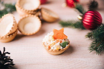 Crab salad tarts on wooden background. Christmas holiday buffet table served by snacks. Red baubles, fir-tree branches. 
