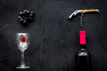 Open wine bottle. Grape, glass and corkscrew on black background top view copyspace
