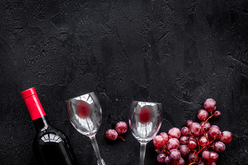 Taste red wine. Bottle of red wine, glass and red grape on black background top view copyspace