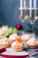 Crab salad tarts on wooden background. Christmas holiday buffet table served by snacks. Red baubles, fir-tree branches. Glass of champagne