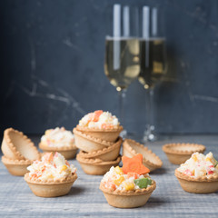 Crab salad tarts on wooden background. Christmas holiday buffet table served by snacks. Red baubles, fir-tree branches. Glass of champagne