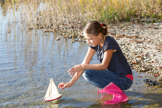 Young girl floating toy boat on water