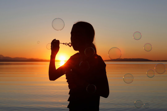 Young girl, outdoors, blowing bubbles, at sunset