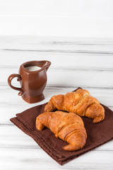Freshly baked croissants on brown napkin, cream in ceramic milk jug on white old wooden background. Fresh pastries for breakfast. Delicious dessert. Closeup photography. Vertical banner