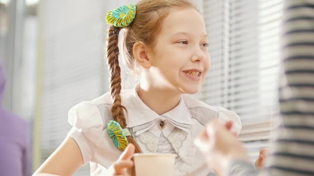 Girl with pigtail is eating sweets in the cafe, talking with her mum and dansing