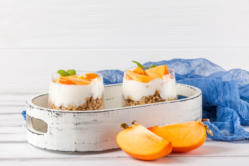 Persimmon creamy trifle in beautiful glasses, fresh ripe fruit slices on white wooden background. Healthy vegetarian food. Delicious dessert. Close up photography. Selective focus.