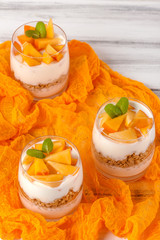 Persimmon creamy trifle in beautiful glasses, fresh ripe fruit slices on white wooden background. Healthy vegetarian food. Delicious dessert. Close up photography. Selective focus.