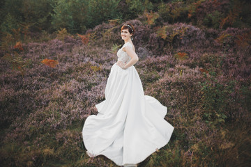 Fototapeta premium Bride in wedding dress posing on grass with beautiful landscape background