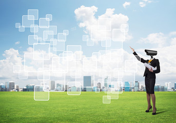 Camera headed woman standing on green grass against modern cityscape