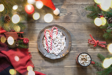 Christmas composition of plate with sweets, cup of coffee, wreath, checkered pleid on wooden board. Flat lay. Top view. Copy space.