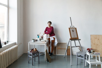 Female artist in her spacious white studio working with watercolor painting.  Natural lighting. Disclosure of creativity concept. Horizontal composition with copy space.