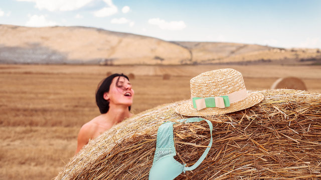 Woman getting undressed behind hay bale