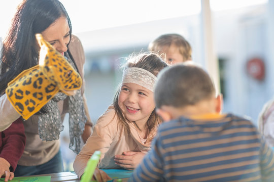 Mid adult woman, wearing hand puppet, standing beside children, laughing