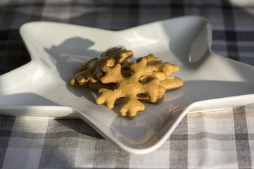 Traditional tasty Czech gingerbreads, Christmas snowflakes on white star shaped plate on grey chequered tablecloth