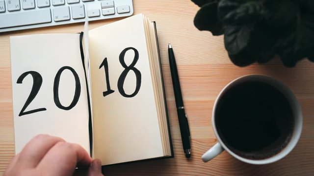 New Year 2018 is coming concept. Hand flips notepad sheet on wooden table. 2017 is turning, 2018 is opening, retro toned