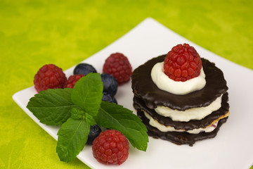 Layers of chocolate biscuits filled with whipped cream and small raspberry pieces and decorated with a sprig of mint and a raspberry on top.