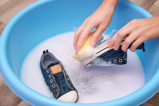 Woman washing sneakers with sponge over plastic basin, closeup