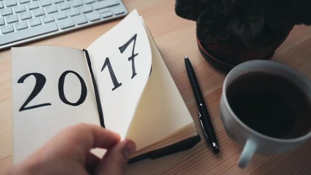 New Year 2018 is coming concept. Hand flips notepad sheet on wooden table. 2017 is turning, 2018 is opening, retro toned