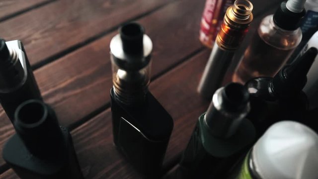 E-cig mods or Electronic cigarettes for vaping on a wooden background. Vape devices and e-liquids in Smoke Cloud of vapour, toned