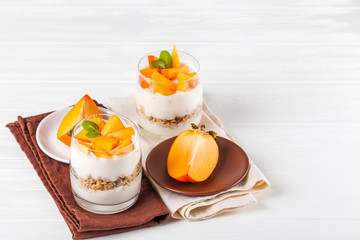Persimmon creamy trifle in beautiful glasses, fresh ripe fruit slices on white wooden background. Healthy vegetarian food. Delicious dessert. Close up photography. Selective focus.