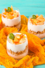 Persimmon creamy trifle in beautiful glasses, fresh ripe fruit slices on mint wooden background. Healthy vegetarian food. Delicious dessert. Close up photography. Selective focus.