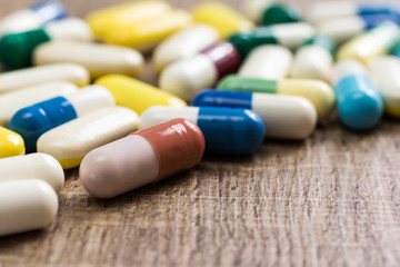 Heap of assorted colorful capsules on wooden background.